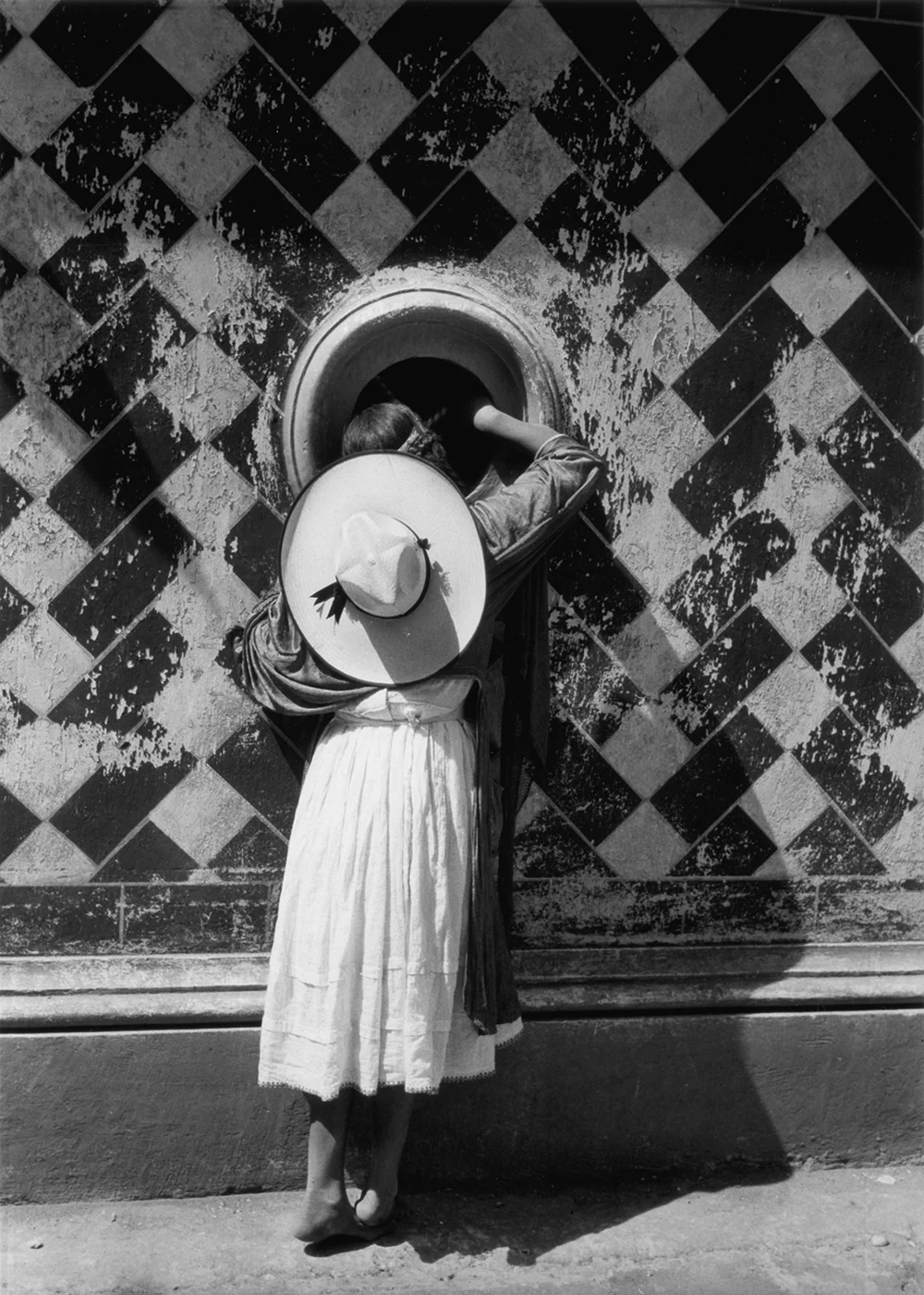 Fotografía en blanco y negro de mujer de espalda mirando a través de un ventanal circular de Manuel Álvarez Bravo titulada La hija de los danzantes de 1933