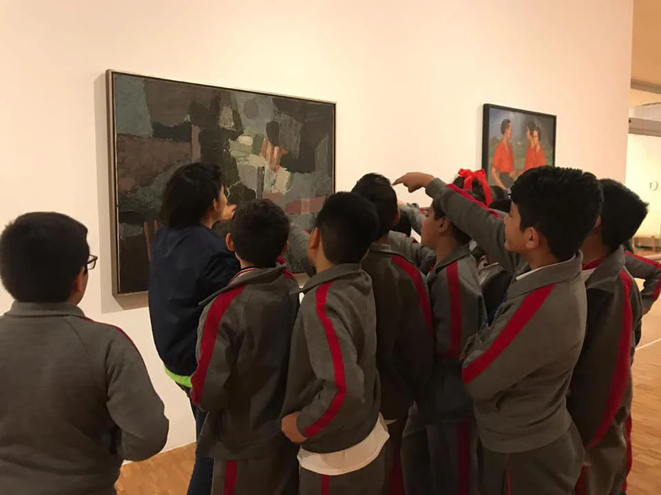 Fotografía de un grupo escolar mirando y conversando frente a una pintura abstracta